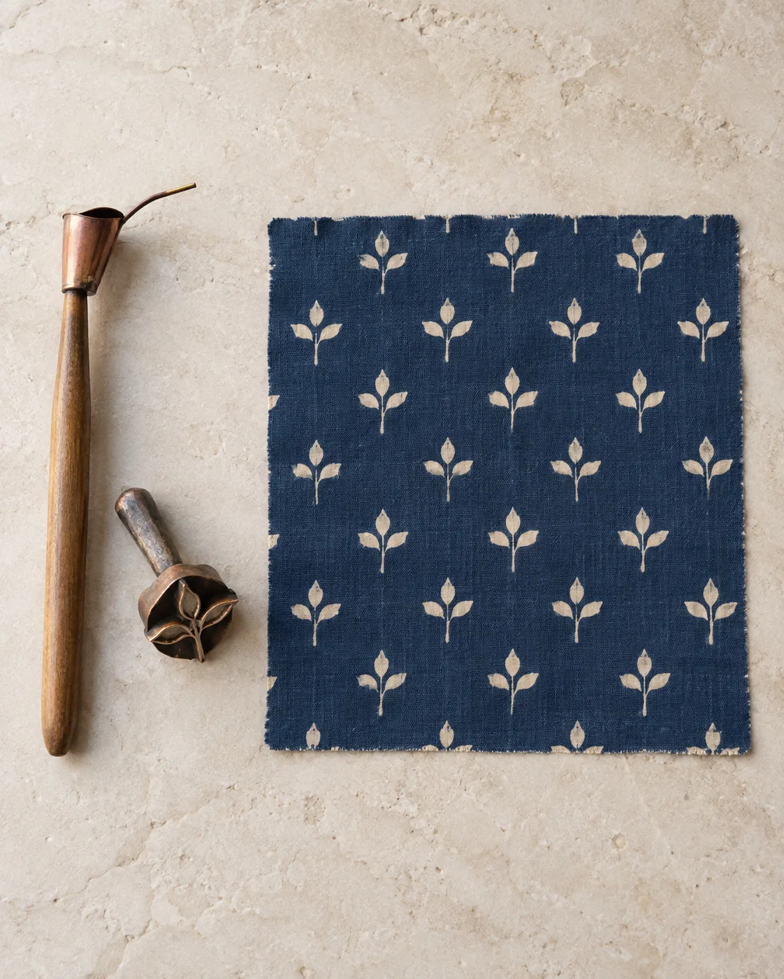 A canting wax pen and metal sprig stamp beside indigo cotton batik with cream sprigs