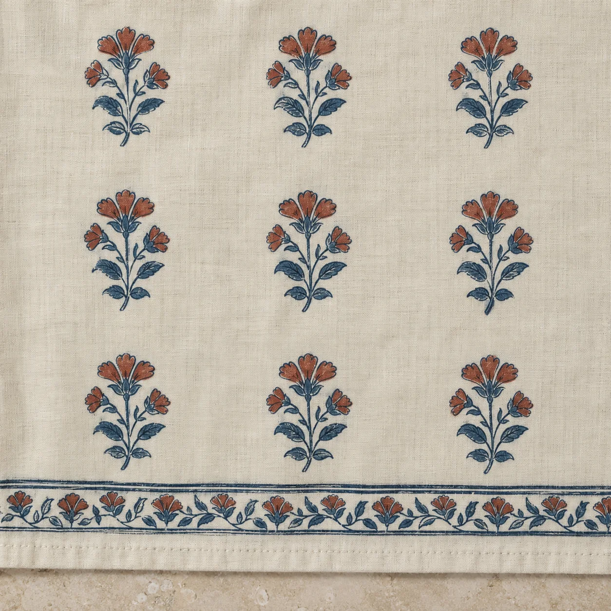 Cream cotton with rows of blue and rust floral motifs and a printed border beside a sewn hem