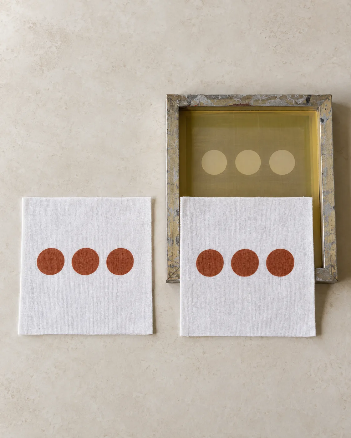 Matching rust circles printed on two white jersey pieces, with a prepared screen behind the right piece