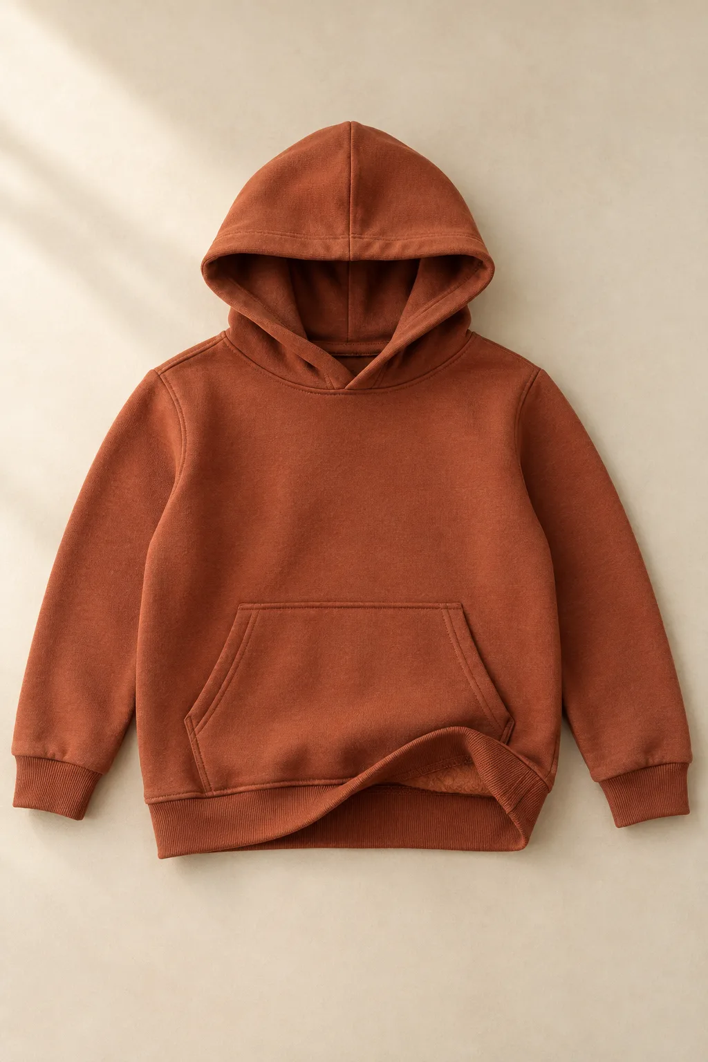 Rust-coloured children’s hoodie with rib cuffs and a turned hem showing the brushed inside
