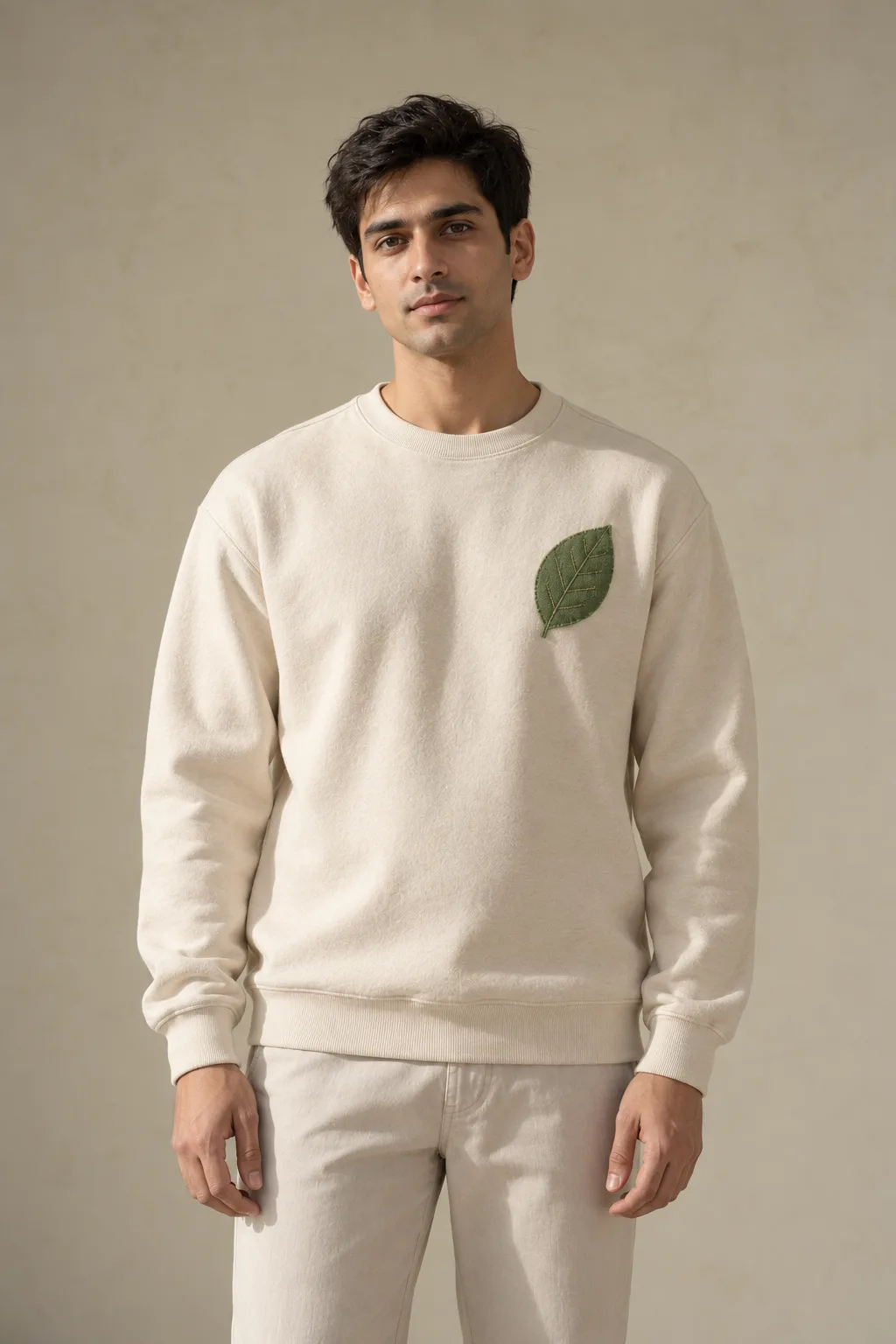 Ecru sweatshirt with an olive fabric leaf stitched onto the chest