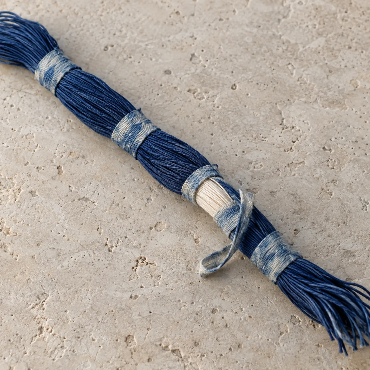 Indigo yarn bundle with tight thread bindings and one opened binding revealing ivory yarn