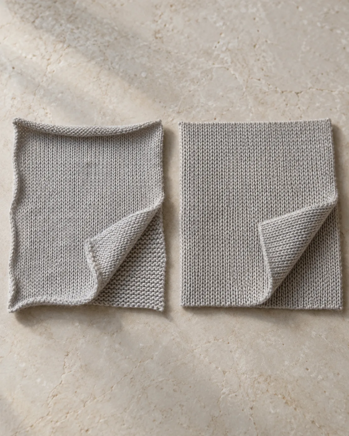 Two grey knit swatches with turned corners: single jersey with curled edges on the left, flat interlock on the right