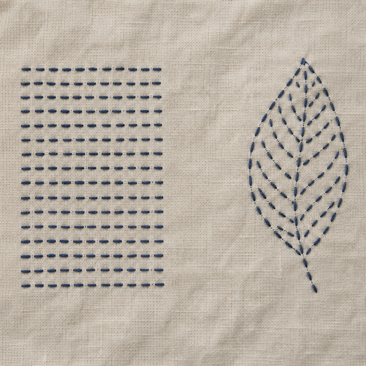 Indigo running-stitch rows beside an outlined and filled leaf on ecru cloth, with unstitched ground between them