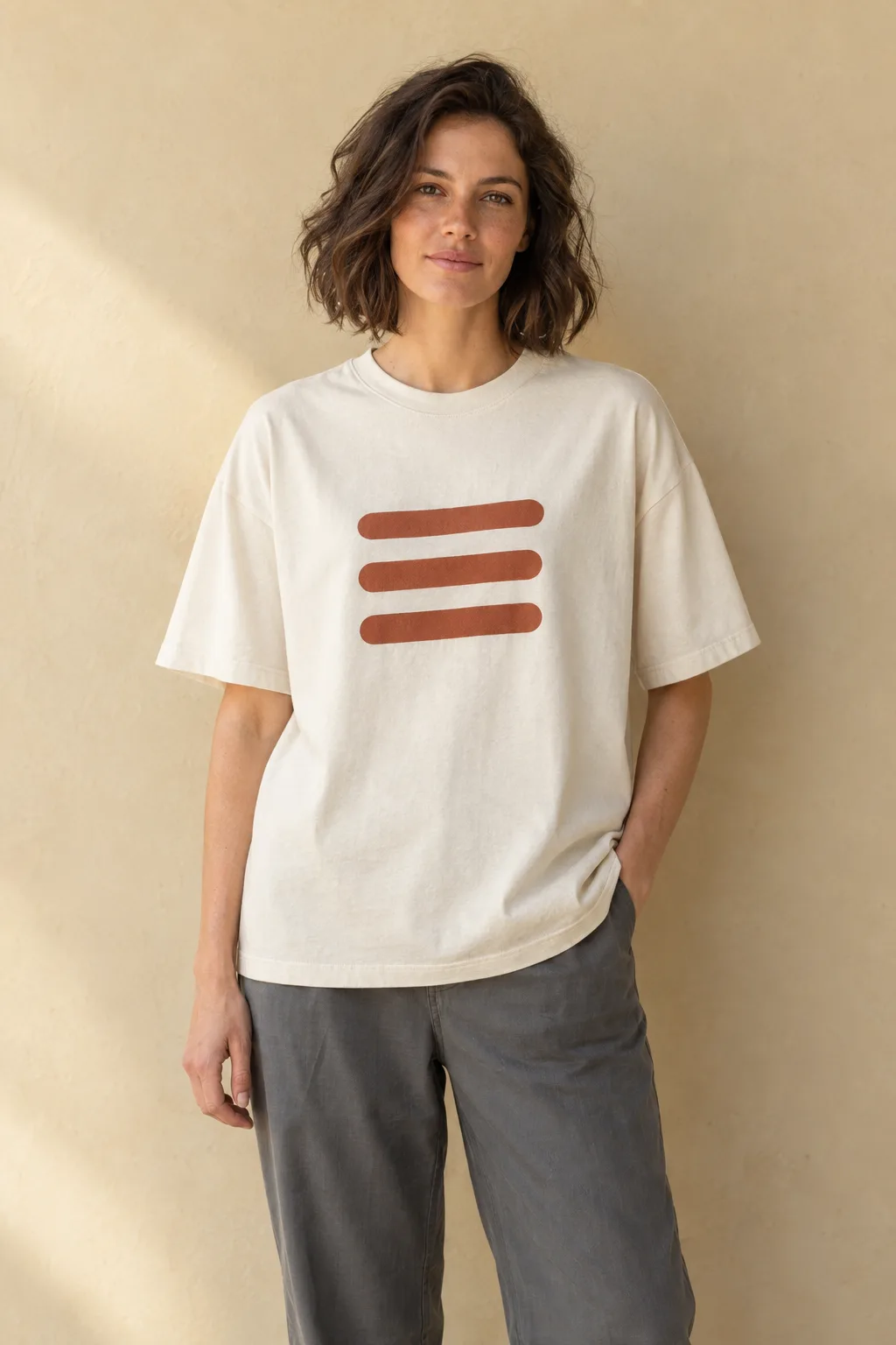 Woman wearing an ecru oversized T-shirt with three rust bars on the chest