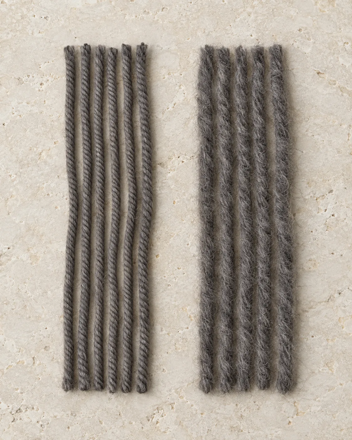 Slate-grey yarn bundles: smooth worsted yarn on the left and bulkier, fuzzy woollen yarn on the right