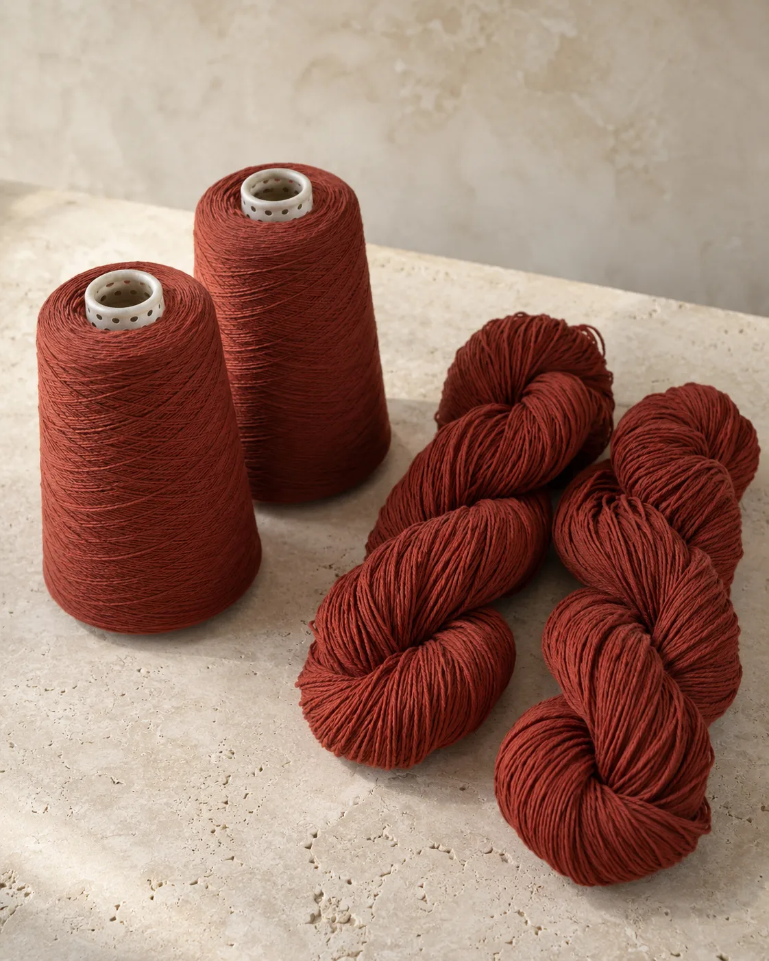 Terracotta yarn on perforated package cores beside two tied hanks